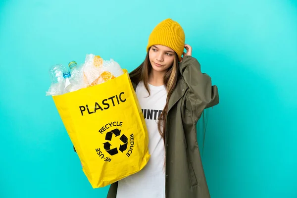 小さな女の子保持バッグフルのプラスチックボトルリサイクル上の隔離された青の背景疑問を持っている — ストック写真