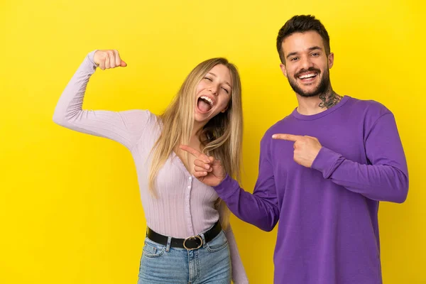 Casal Jovem Sobre Fundo Amarelo Isolado Fazendo Gesto Forte — Fotografia de Stock