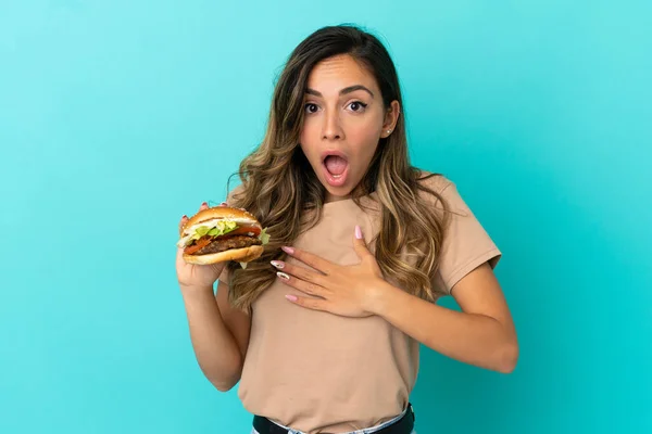 Młoda Kobieta Trzyma Hamburgera Odosobnionym Tle Zaskoczony Zszokowany Patrząc Prawo — Zdjęcie stockowe