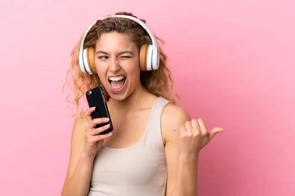 분홍색 배경에 고립된 여자가 핸드폰으로 음악을 노래를 부른다 — 스톡 사진