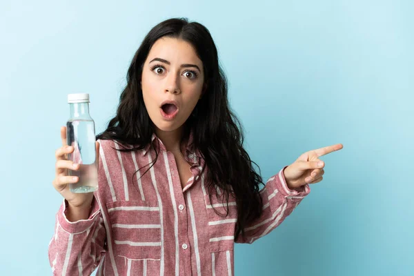 Jovem Com Uma Água Isolada Fundo Azul Surpreendido Apontando Lado — Fotografia de Stock