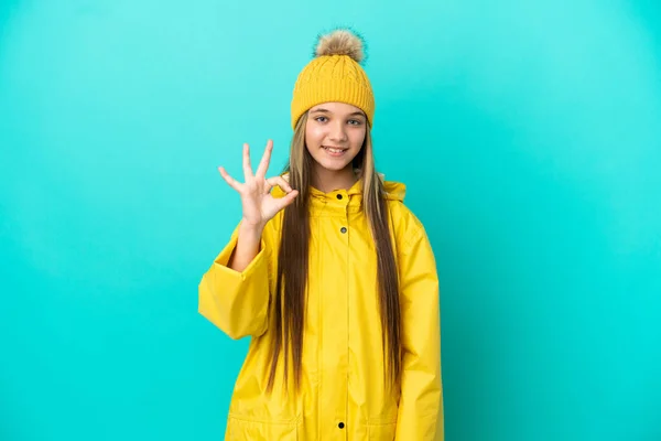 Niña Usando Abrigo Impermeable Sobre Fondo Azul Aislado Mostrando Signo —  Fotos de Stock