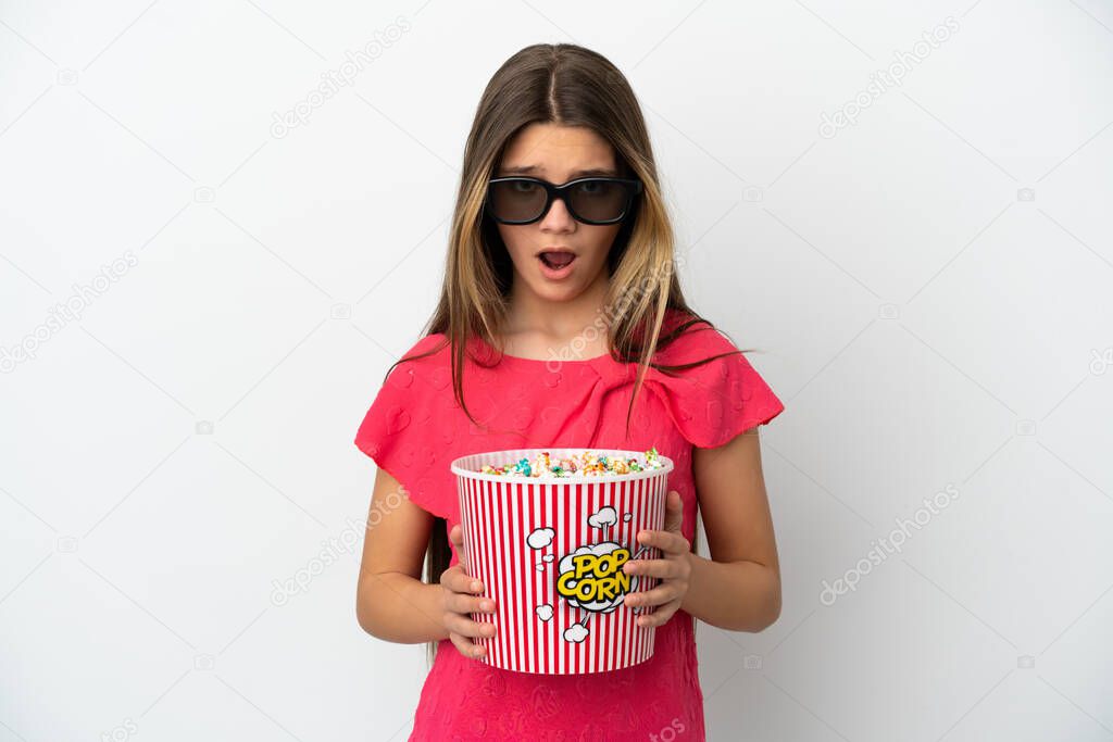 Little girl over isolated white background surprised with 3d glasses and holding a big bucket of popcorns