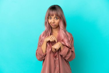 Mavi arka planda pembe saçlı melez bir kadın geç kalma jesti yapıyor.