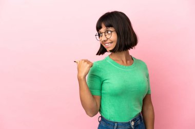 Pembe arka planda izole edilmiş genç melez kadın bir ürünü sunmak için kenarı işaret ediyor.