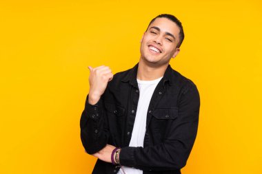 Asyalı yakışıklı adam sarı arka planda izole edilmiş, dur hareketi yapıyor.