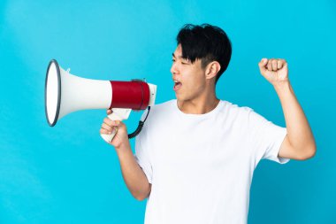 Mavi arka planda izole edilmiş genç bir Çinli megafonla bir şey duyurmak için bağırıyor.