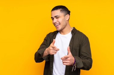 Asyalı yakışıklı adam sarı arka planda izole edilmiş harika bir fikre işaret ediyor.