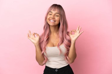 Pembe saçlı melez kadın pembe arka planda Zen pozisyonunda.