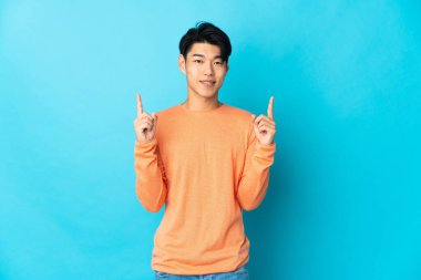 Mavi arka planda izole edilmiş genç bir Çinli harika bir fikre işaret ediyor.