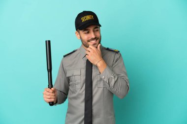 Mavi arka planda izole edilmiş genç bir güvenlik görevlisi yana bakıyor ve gülümsüyor.