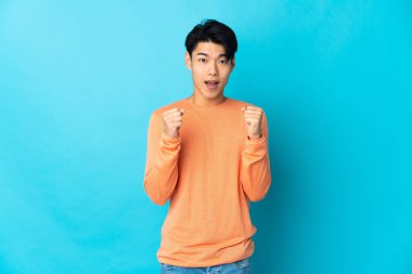 Genç Çinli adam mavi arka planda tek başına zaferi kutluyor.