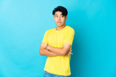 Mavi arka planda izole edilmiş genç bir Çinli omuzlarını kaldırırken şüphe jesti yapıyor.