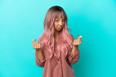 Mavi arka planda izole edilmiş pembe saçlı melez bir kadın para hareketi yapıyor.