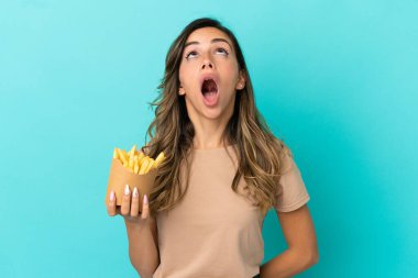 Kızarmış cipsleri izole edilmiş arka planda tutan genç bir kadın yukarı bakıyor ve şaşırmış bir ifadeyle