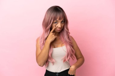 Pembe saçlı melez bir kadın pembe arka planda bir şey gösteriyor.