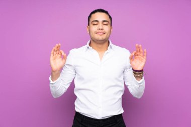 Asyalı yakışıklı adam mavi arka planda Zen pozuyla izole edilmiş.