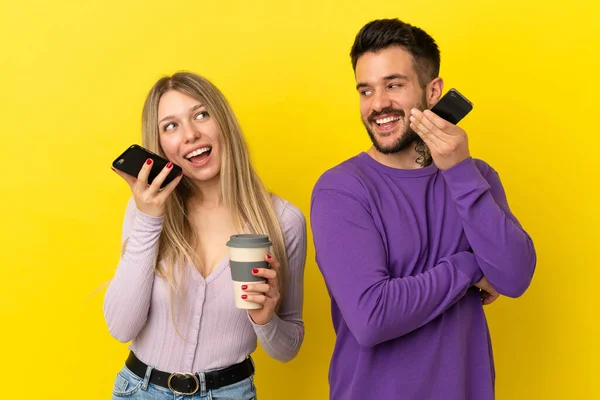 来自孤立的黄色背景的年轻夫妇用手机发送消息 语音或电子邮件 — 图库照片