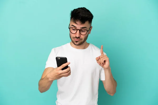 Genç Beyaz Adam Mavi Arka Planda Cep Telefonu Parmak Kaldırarak — Stok fotoğraf