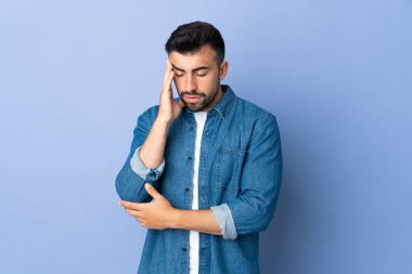 Kafkasyalı adam mavi arka planda, baş ağrısı var.