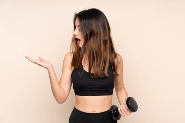 Bej arka planda izole haldeki halter kaldıran genç spor kadını, el bilgisayarında hayali bir kopya alanı tutuyor.