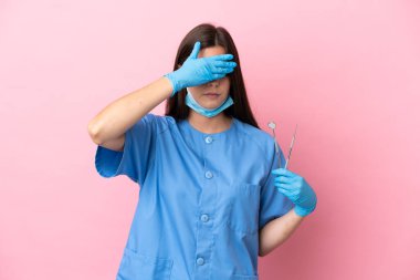 Dentist woman holding tools isolated on pink background covering eyes by hands. Do not want to see something