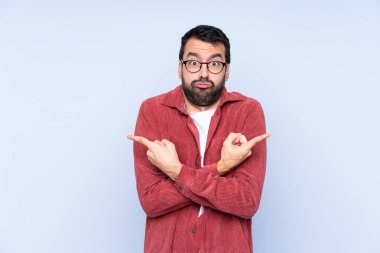 Young caucasian man wearing corduroy jacket over blue background pointing to the laterals having doubts