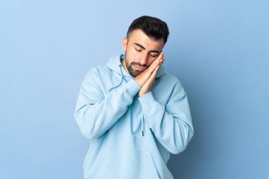 İzole edilmiş mavi arka plan üzerinde beyaz bir adam uyku jesti yapıyor.