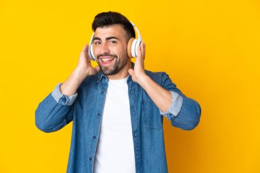 İzole edilmiş sarı arka planda beyaz bir adam müzik dinliyor.