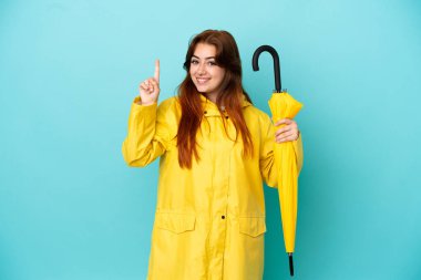 Mavi arka planda şemsiye tutan kızıl saçlı kadın en iyinin işareti olarak parmağını kaldırıyor ve gösteriyor.
