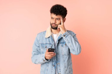 Young Moroccan man using mobile phone isolated on pink background thinking an idea