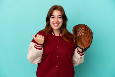 Beyzbol oynayan genç kızıl saçlı kadın, mavi arka planda soyutlanmış bir şekilde bir ürünü sunmak için kenarı işaret ediyor.