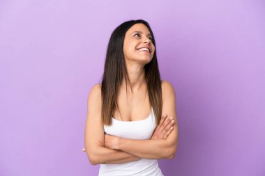 Mor arka planda izole edilmiş genç beyaz kadın gülümserken yukarı bakıyor.