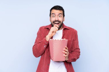 Mavi arka planda beyaz bir adam elinde koca bir kova patlamış mısır tutuyor.