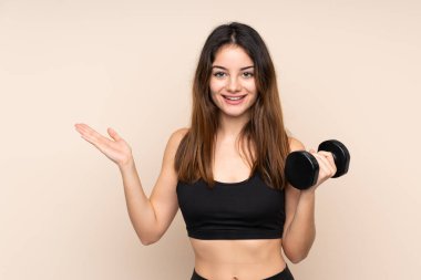 Genç bayan halter bej arka planda yalıtılmış halter yapıyor. Davet için ellerini yana uzatıyor.