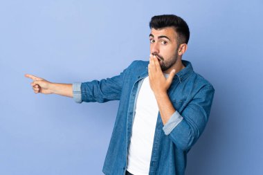 İzole edilmiş mavi arka planda beyaz bir adam sürpriz bir ifadeyle işaret ederken...