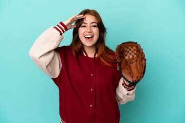 Beyzbol oynayan genç kızıl saçlı kadın mavi arka planda yalnız ve sürpriz bir ifadeyle.