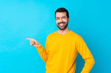 Young caucasian man over isolated blue background pointing finger to the side