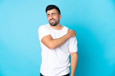 İzole edilmiş mavi arka planda beyaz bir adam omuz ağrısından muzdarip.