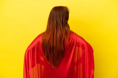 Süper kahraman kızıl saçlı kadın sarı arka planda izole edilmiş.