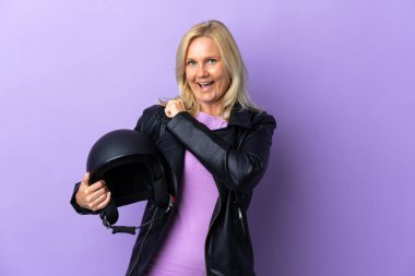 Mor arka planda motosiklet kaskı tutan orta yaşlı bir kadın zaferi kutluyor.