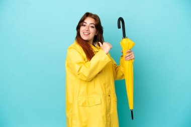 Mavi arka planda şemsiyesi olan kızıl saçlı kadın gururlu ve kendini beğenmiş.