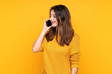 Sarı arka planda izole edilmiş genç beyaz kadın cep telefonuyla sohbet ediyor.