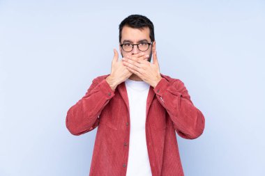Young caucasian man wearing corduroy jacket over blue background covering mouth with hands