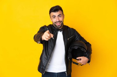 Motosiklet kasklı beyaz adam izole edilmiş sarı arka planda mutlu bir ifadeyle ön tarafı işaret ediyor.