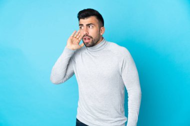 İzole edilmiş mavi arka planda beyaz bir adam. Kulağına elini sürerek bir şeyler dinliyor.