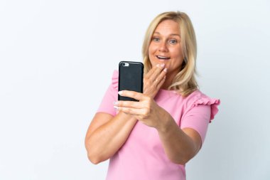 Beyaz arka planda izole edilmiş, şaşırmış ve şok olmuş bir yüz ifadesi olan orta yaş cep telefonu kullanımı