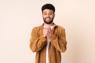 Faslı genç bir adam bej arka planda izole edilmiş gülüyor.