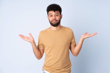 Faslı genç bir adam mavi arka planda izole edilmiş şüpheli hareketlerde bulunuyor.