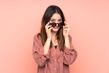 Pembe arka planda gözlüklü ve şaşırmış genç beyaz kadın.